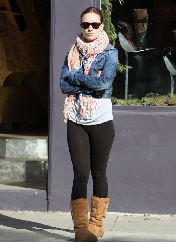 A woman wearing a chunky scarf, denim jacket, thick black leggings and tan coloured Ugg style boots