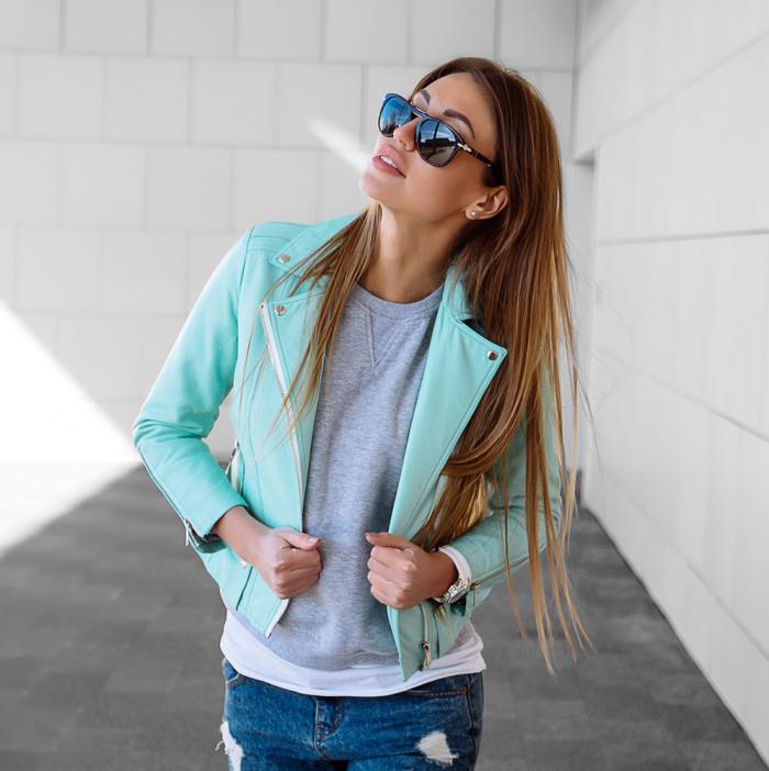 Модель в солнцезащитных очках, кожаной куртке и джинсах темно-синего цвета