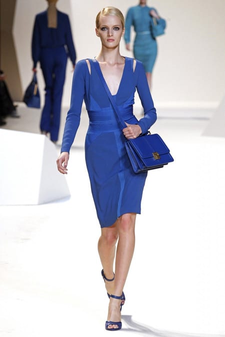 На модели синее платье с длинными рукавами и сумочка в тон