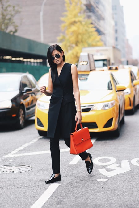 Модель в черных брюках, удлиненный кардиган без рукавов, оранжевая сумка