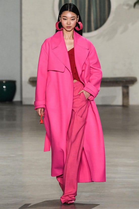 Модель в розовых широких брюках, красный топ и розовое пальто