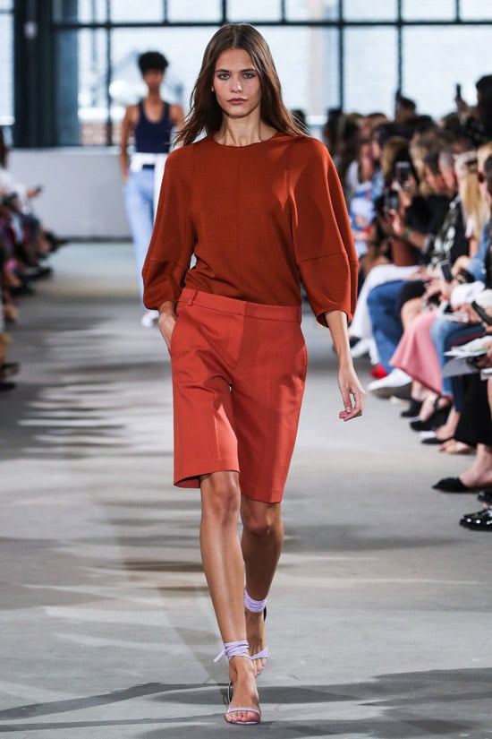 Модель в оранжевых шортах бермудах, свитшот и красивые босоножки