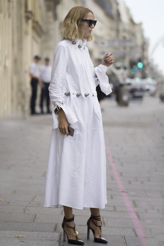 Белая длинная рубашка свободного кроя с металлическими пуговицами модно выглядит с черными лаковыми туфлями на высоком каблуке.